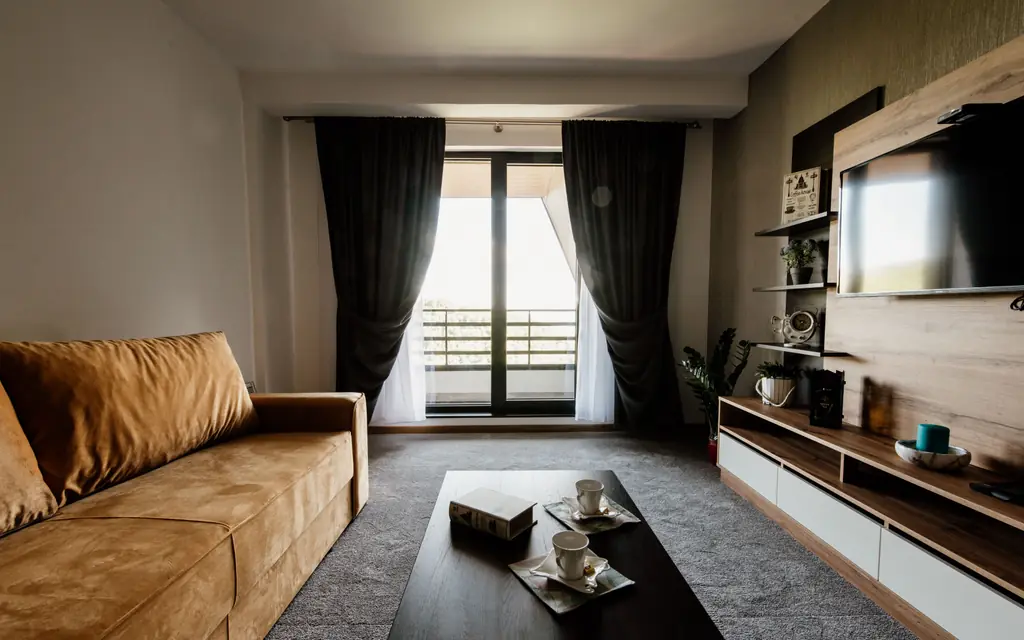 Wohnzimmer mit Sofa, Holzregal und bodentiefer Tür zum Balkon